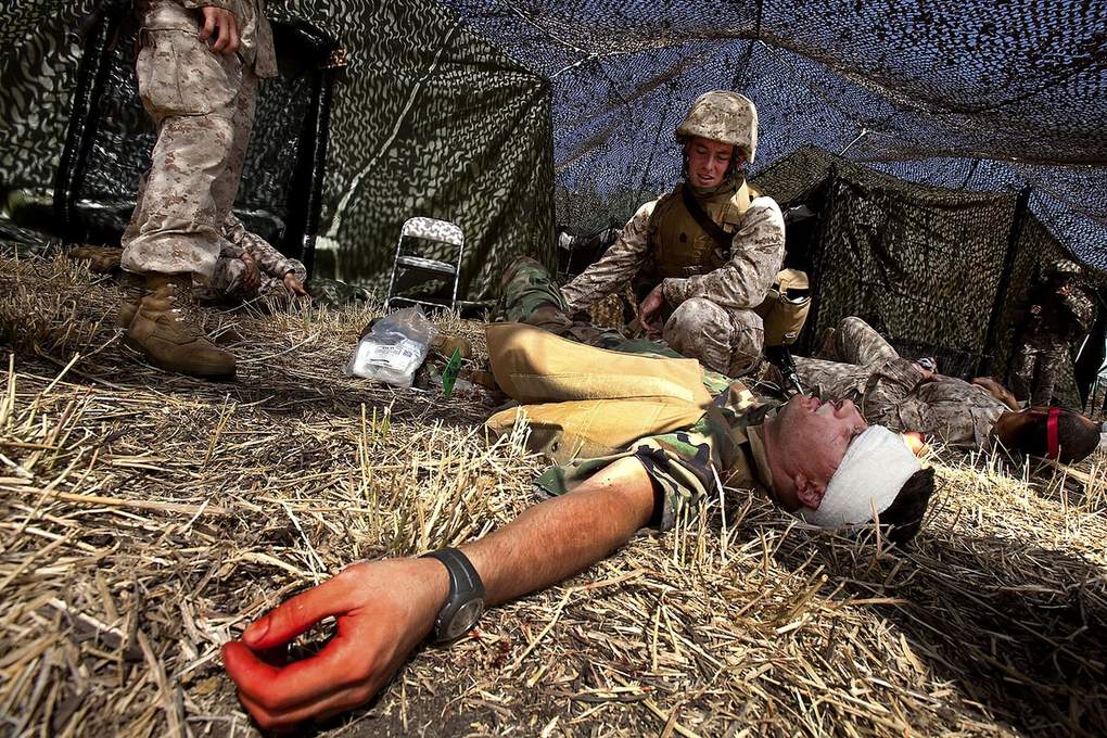A soldier lying on straw with a thick bandage wrapped around his forearm