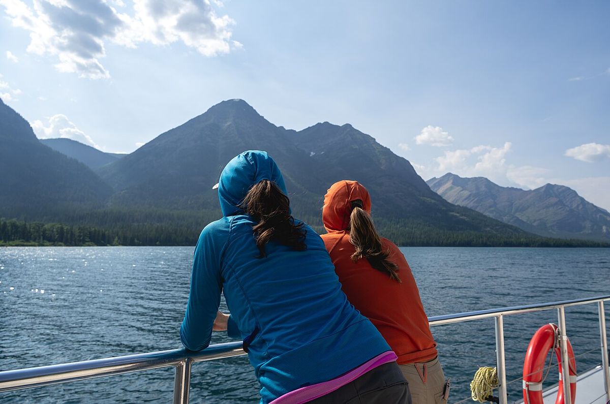 Two people in hooded fleece and jackets looking out over a mountain lake