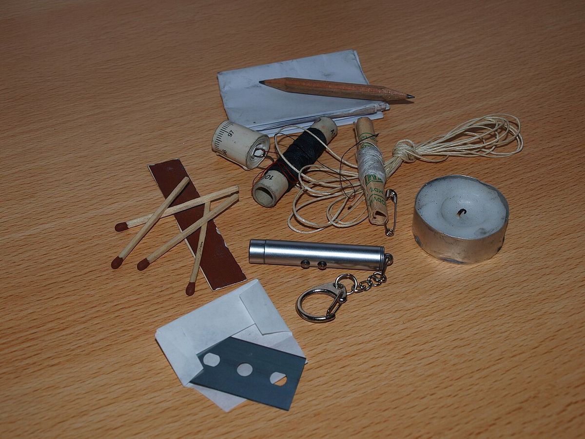 A small pocket survival kit laid out: matches, candle, cord, wire, blade and tin