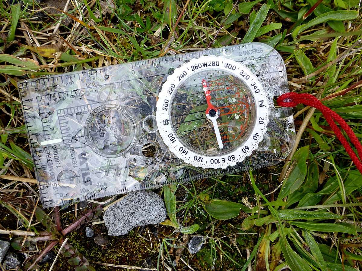 A baseplate compass lying on a folded map in the grass