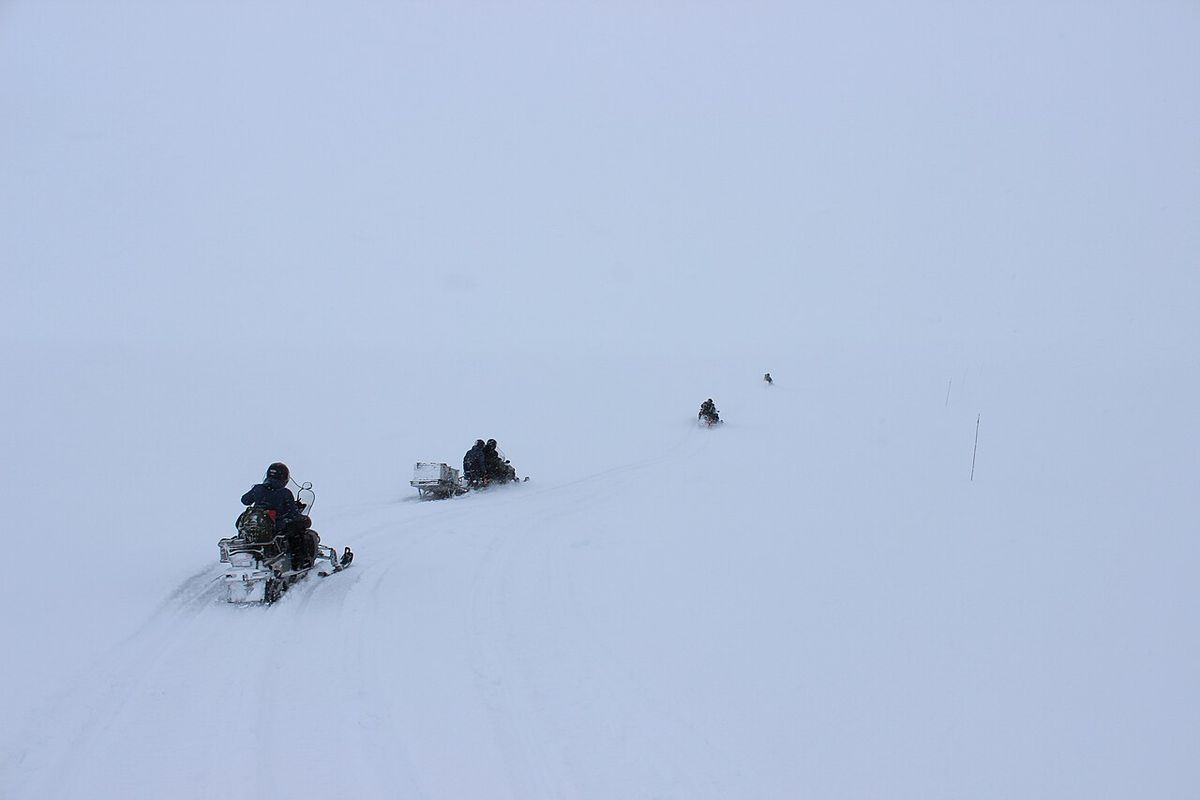 Figures barely visible on a snowmobile in blowing snow and whiteout