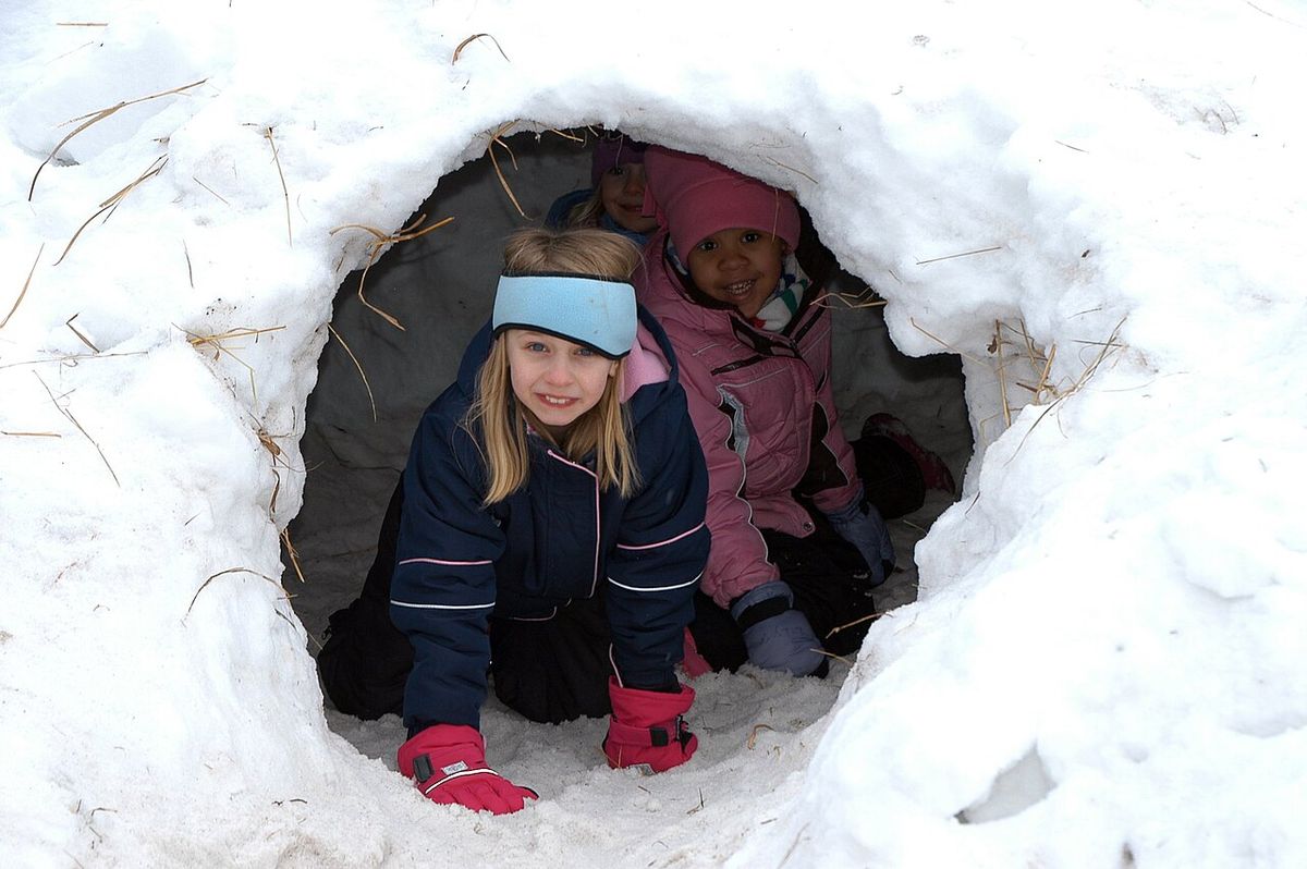 Two children looking out of a small arched snow cave entrance