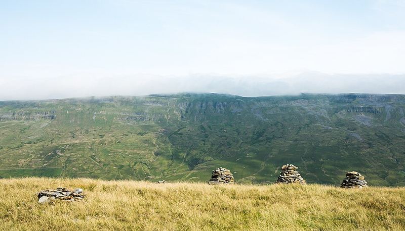 Three stone cairns standing in a row on a grassy hilltop