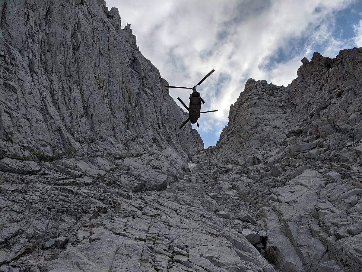 A helicopter hovering above a steep rocky gully with a litter on the hoist line