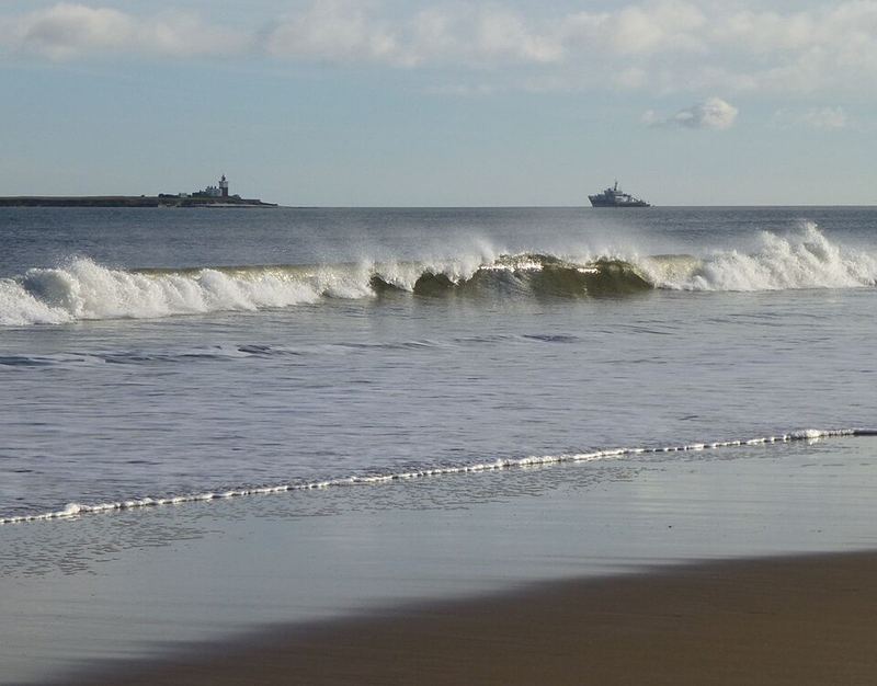 A wave breaking on a sandy beach with the open sea behind